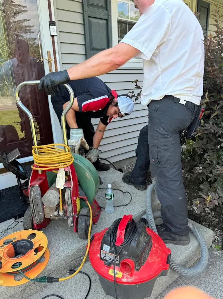 Two plumbers clearing a drain line at a customer's front door